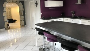 Et moderne køkken med en central ø, barstole, indbygget ovn og et emfang i rustfrit stål.