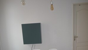 A dining area with a wooden table, four white chairs, two pendant lights, and a wall-mounted television. - Casa Estrella - Marseille hypercentre ❤️ (Marseille)