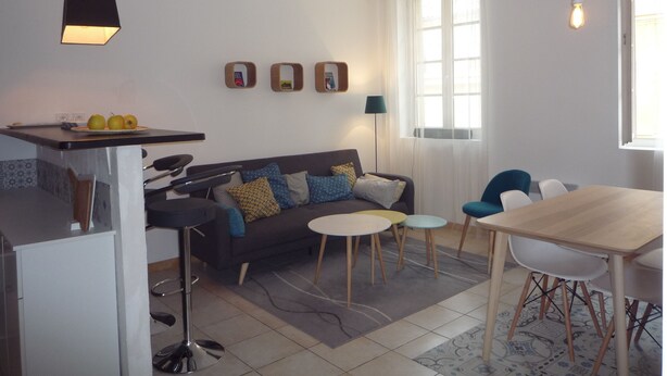 A modern living room with a sofa, coffee table, and dining area. There are three framed pictures on the wall, a lamp, and a window with curtains. - Casa Estrella - Marseille hypercentre ❤️ (Marseille)