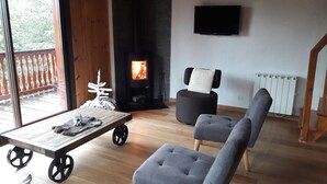 A living room with a fireplace, a television mounted on the wall, and a view of the outdoors through large windows. - Very pretty semi-detached chalet, all comforts, close to the Chantemerle slopes  (Saint-Chaffrey)