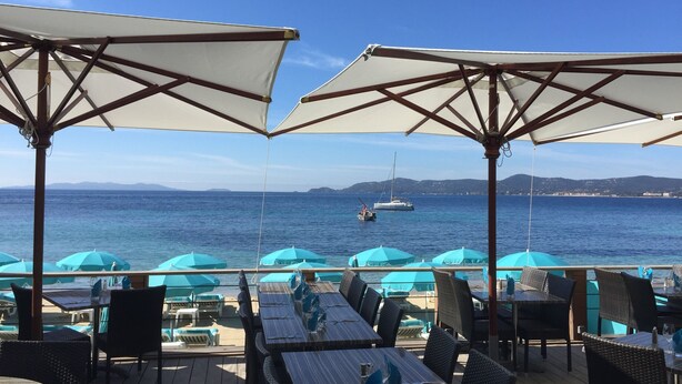 An outdoor dining area with tables and chairs, umbrellas, and a view of the sea. - MAZET with superb sea view and beautiful terrace - 500 m beach (Rayol-Canadel-Sur-Mer)