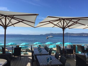 An outdoor dining area with tables and chairs, umbrellas, and a view of the sea. - MAZET with superb sea view and beautiful terrace - 500 m beach (Rayol-Canadel-Sur-Mer)