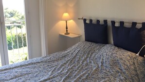A bedroom with a bed, a nightstand with a lamp, and a view of greenery outside. - MAZET with superb sea view and beautiful terrace - 500 m beach (Rayol-Canadel-Sur-Mer)