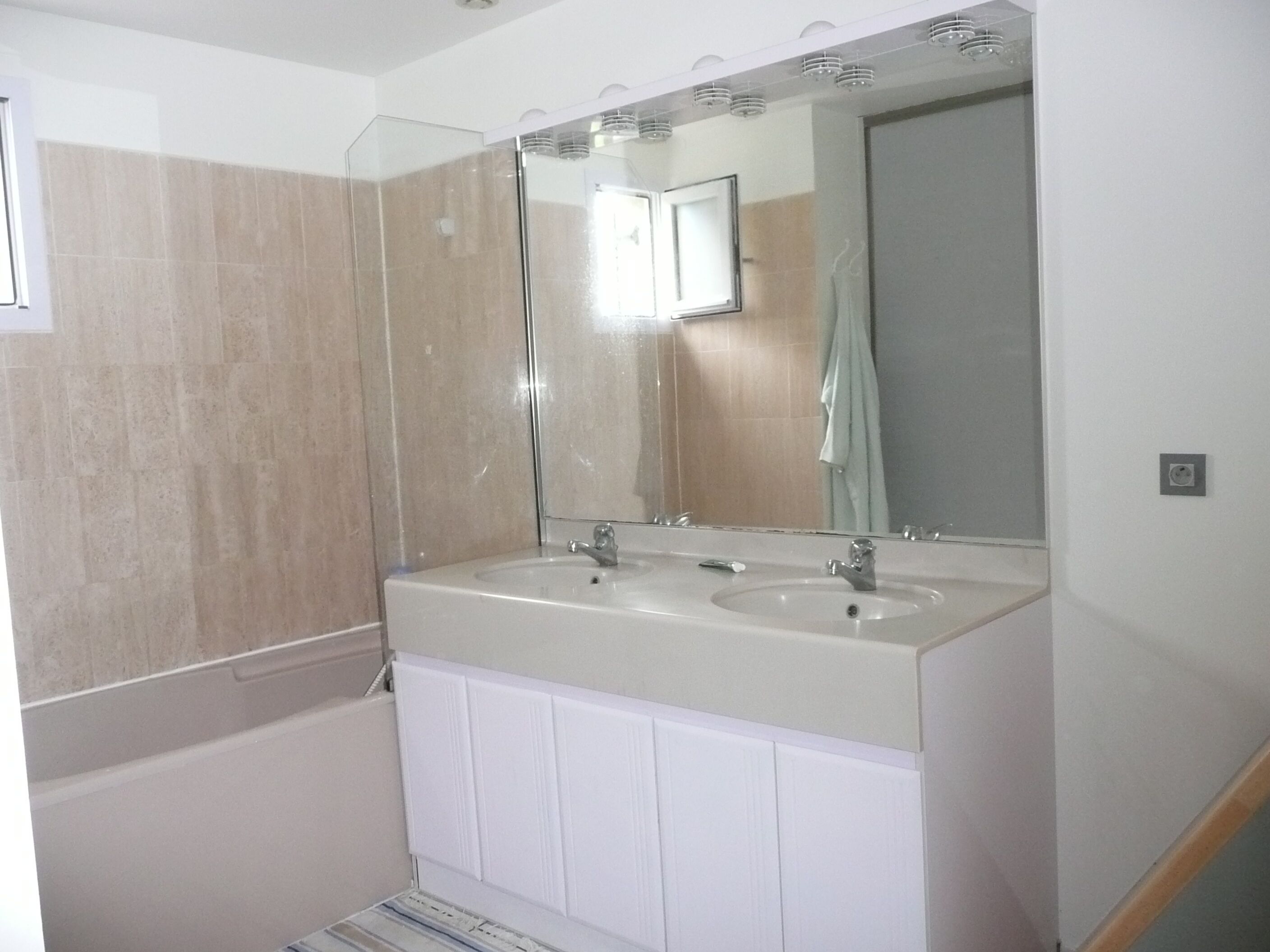 Un baño con lavamanos doble, un espejo grande y cabina de ducha.