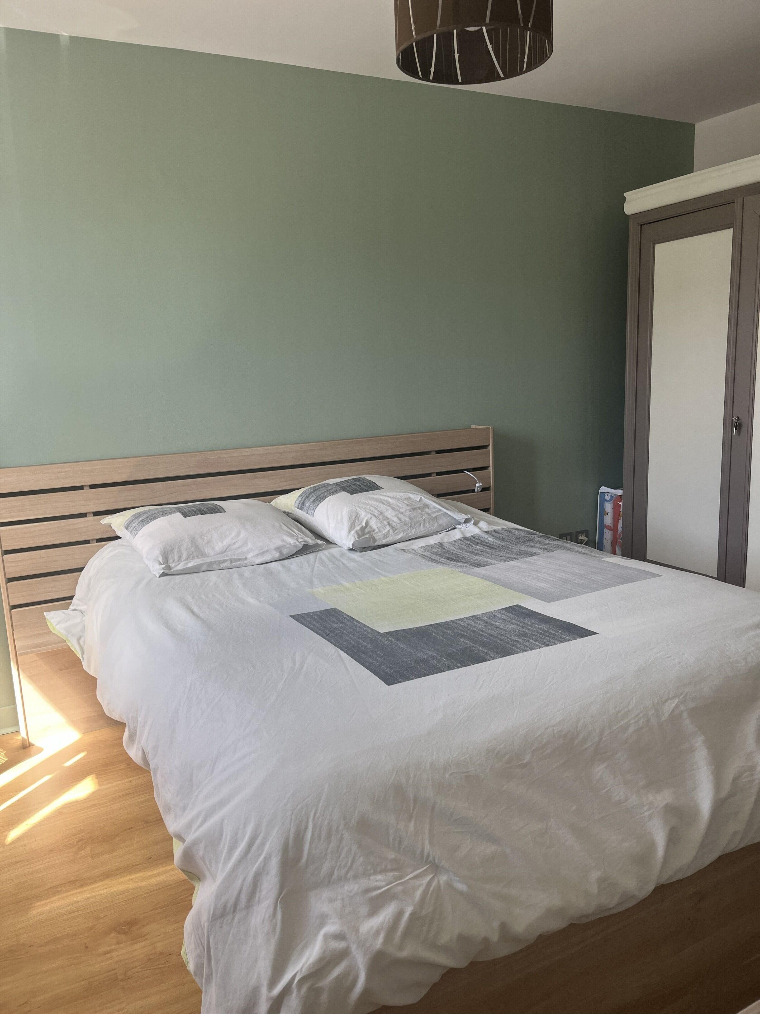Un lit bien fait, avec une tête de lit en bois, une petite table de chevet et une armoire à porte.