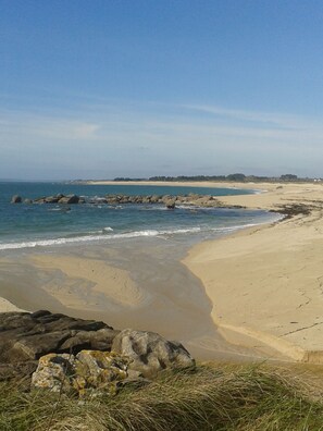 Una platja amb cel blau, sorra daurada i roques grans a l'aigua.