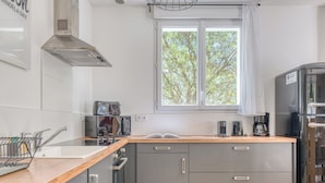 Una cocina moderna con encimera de madera, electrodomésticos de acero inoxidable, armarios grises y ventana con vista a árboles.