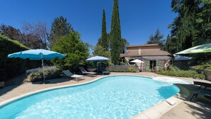 A swimming pool with lounge chairs and umbrellas, surrounded by trees and a building. - Nyons, charming villa in a green setting  (Nyons)