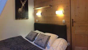 Ett sovrum med en sänggavel i trä, två kuddar med en retrodesign, en tavla med ett rådjur på väggen och två vägglampor.