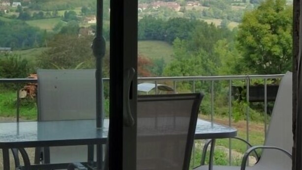 A balcony with a table and chairs, a large umbrella, and a scenic view of a hilly landscape. - Cottage at the Mirande farm near Rocamadour, Padirac, Collonges la rouge (Queyssac-Les-Vignes)