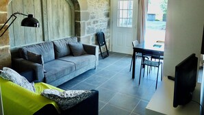 A living area with a stone wall, a sofa, a dining table with chairs, and a television.