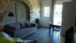 A cozy living room with a stone wall, a grey sofa, a dining table with chairs, and a ceiling fan. - Cottage at the Mirande farm near Rocamadour, Padirac, Collonges la rouge (Queyssac-Les-Vignes)
