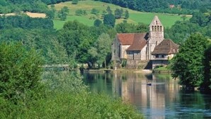 A historic building with a tower, situated by a calm river, surrounded by lush greenery. - Cottage at the Mirande farm near Rocamadour, Padirac, Collonges la rouge (Queyssac-Les-Vignes)