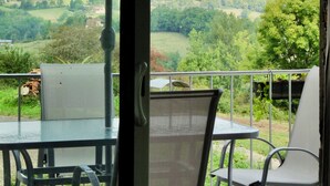 A balcony with a table and chairs, an umbrella, and a view of a green landscape with hills.