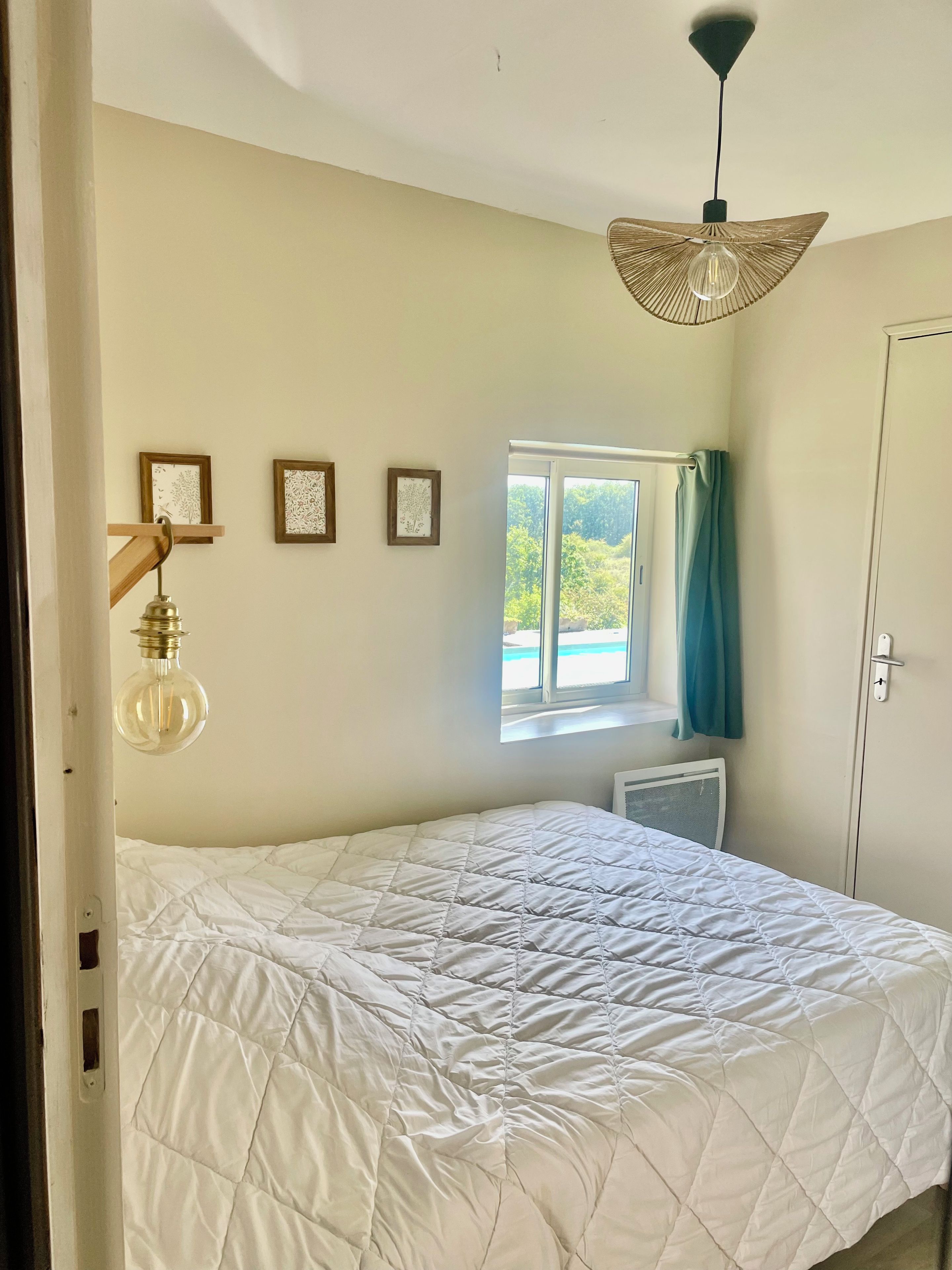 A bedroom with a bed, a window with curtains, a radiator, and wall-mounted light fixtures.