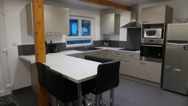 A modern kitchen with a central island, stainless steel appliances, and a window with a view. - Modern gîte in Alsace (Lutzelhouse)
