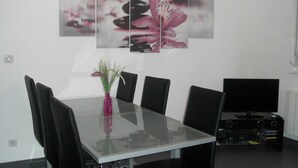 A modern dining area with a glass table, black chairs, a pink vase with plants, and a flat-screen TV on a stand. - Modern gîte in Alsace (Lutzelhouse)