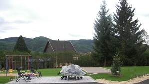 A covered outdoor seating area with a swing set and a covered table in a park-like setting with hills in the background. - Modern gîte in Alsace (Lutzelhouse)