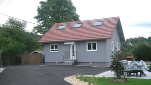 A two-story house with a red-tiled roof, a grey exterior, and a front entrance with steps. - Modern gîte in Alsace (Lutzelhouse)