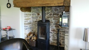 A rustic room with a stone wall, a wood-burning stove, a lamp, and a chair. - Gîte for 6 people with heated indoor pool - Gîtes de France 5 épis (Carentoir)