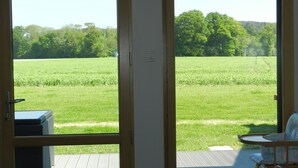 A room with a sliding glass door leading to a deck with a view of a green field and trees. - Gîte for 6 people with heated indoor pool - Gîtes de France 5 épis (Carentoir)