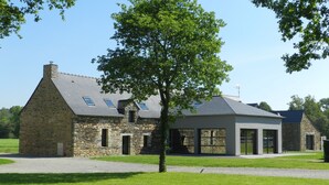 A stone building with a sloped roof, large windows, and a covered outdoor area. - Gîte for 6 people with heated indoor pool - Gîtes de France 5 épis (Carentoir)