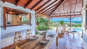 Un espacio de comedor al aire libre cubierto con vista al océano, mobiliario de madera y una piscina.