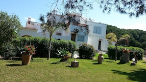 A two-story house with a white exterior, surrounded by well-maintained lawns and various potted plants. - Villa MALYMA direct beach access (Zahora)