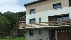 Ein zweigeschossiges Haus mit einer Steinaußenwand, einem hölzernen Balkon und einer Steintreppe, die zu einem Holzboden führt.