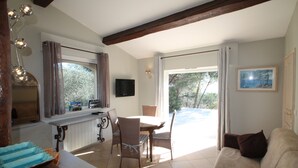 A dining area with a table and chairs, a television on the wall, and a view of the outdoors. - In Tourettes-sur-Loup, charming gite with infinity pool (Tourrettes-Sur-Loup)