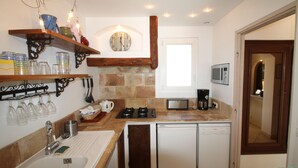 A compact kitchen with a sink, stove, microwave, and a small refrigerator. There are shelves with glassware and a clock on the wall. - In Tourettes-sur-Loup, charming gite with infinity pool (Tourrettes-Sur-Loup)