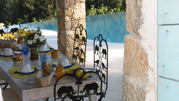 An outdoor dining area with a stone archway, a table set for a meal, and a metal animal-shaped decoration. - In Tourettes-sur-Loup, charming gite with infinity pool (Tourrettes-Sur-Loup)