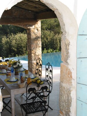 An outdoor dining area with a stone archway, a table set for a meal, and a metal animal-shaped decoration. - In Tourettes-sur-Loup, charming gite with infinity pool (Tourrettes-Sur-Loup)