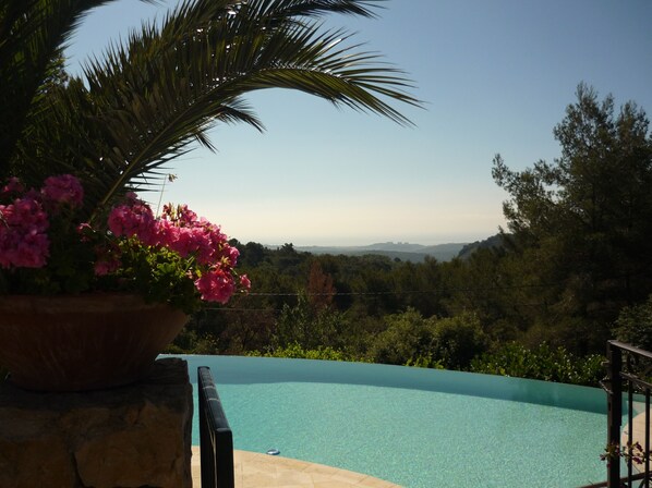 A swimming pool with a clear view of the surrounding landscape, including trees and distant hills. - In Tourettes-sur-Loup, charming gite with infinity pool (Tourrettes-Sur-Loup)