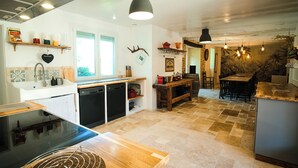 A modern kitchen with a dishwasher, stove, and wooden countertops. There is a dining area with a table and chairs, and a mural on the wall. - Exclusive Hamlet and XXL Pool (Vergt)
