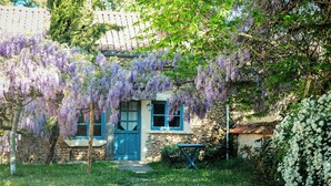 A traditional stone house with a blue door and windows, surrounded by lush greenery and purple wisteria vines. - Exclusive Hamlet and XXL Pool (Vergt)