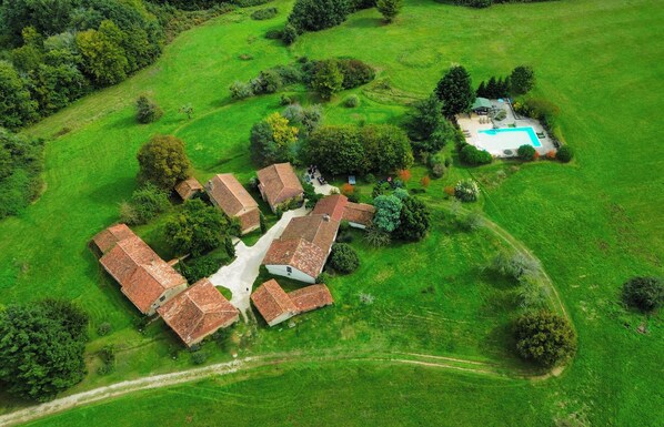 Luchtbeeld van een landelijk gelegen bezit met meerdere gebouwen, een zwembad en omliggende groene velden.