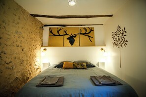 Een slaapkamer met een rustieke stenen muur, een bed met blauw beddengoed, een kunstwerk van een herten boven het bed en twee wandlampen.
