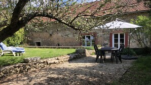 A stone building with a red-tiled roof, a gravel patio, and a table with chairs. - Mansion (Saint-Germain-Des-Champs)