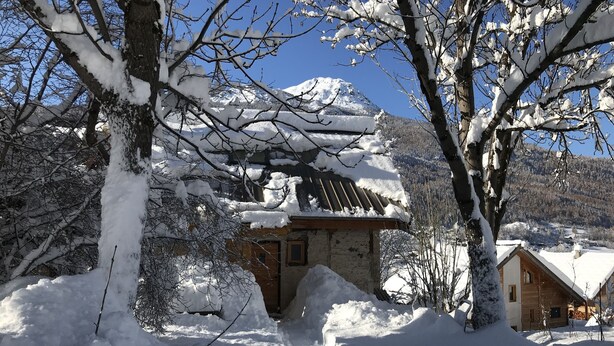 Een met sneeuw bedekte berg met een houten hutje en een huis op de voorgrond.