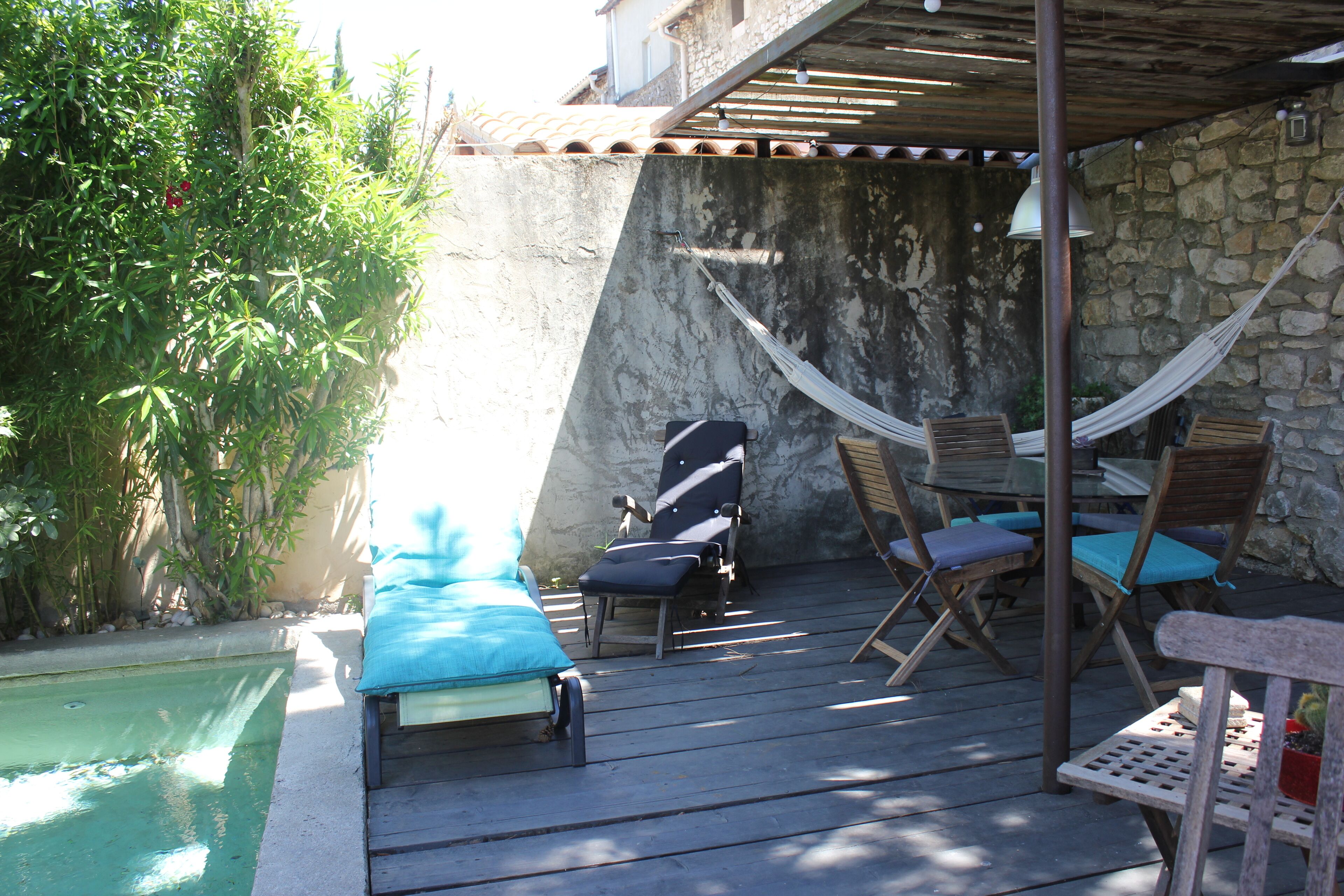 Una terraza de madera con piscina, sillones de descanso y una hamaca.