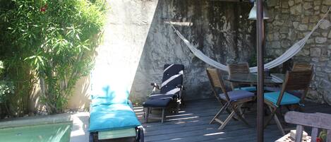 Una terraza de madera con piscina, sillones de descanso y una hamaca.