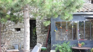 Un edificio de piedra con terraza de madera, asientos exteriores y plantas en macetas.