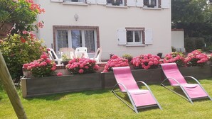 A building with a garden area featuring pink chairs and vibrant flowers.