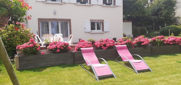 A building with a garden area featuring pink chairs and vibrant flowers.