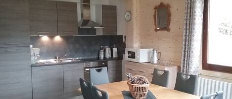 Een moderne keuken met grijze kastjes, een houten eettafel en een mand met dennenappels.