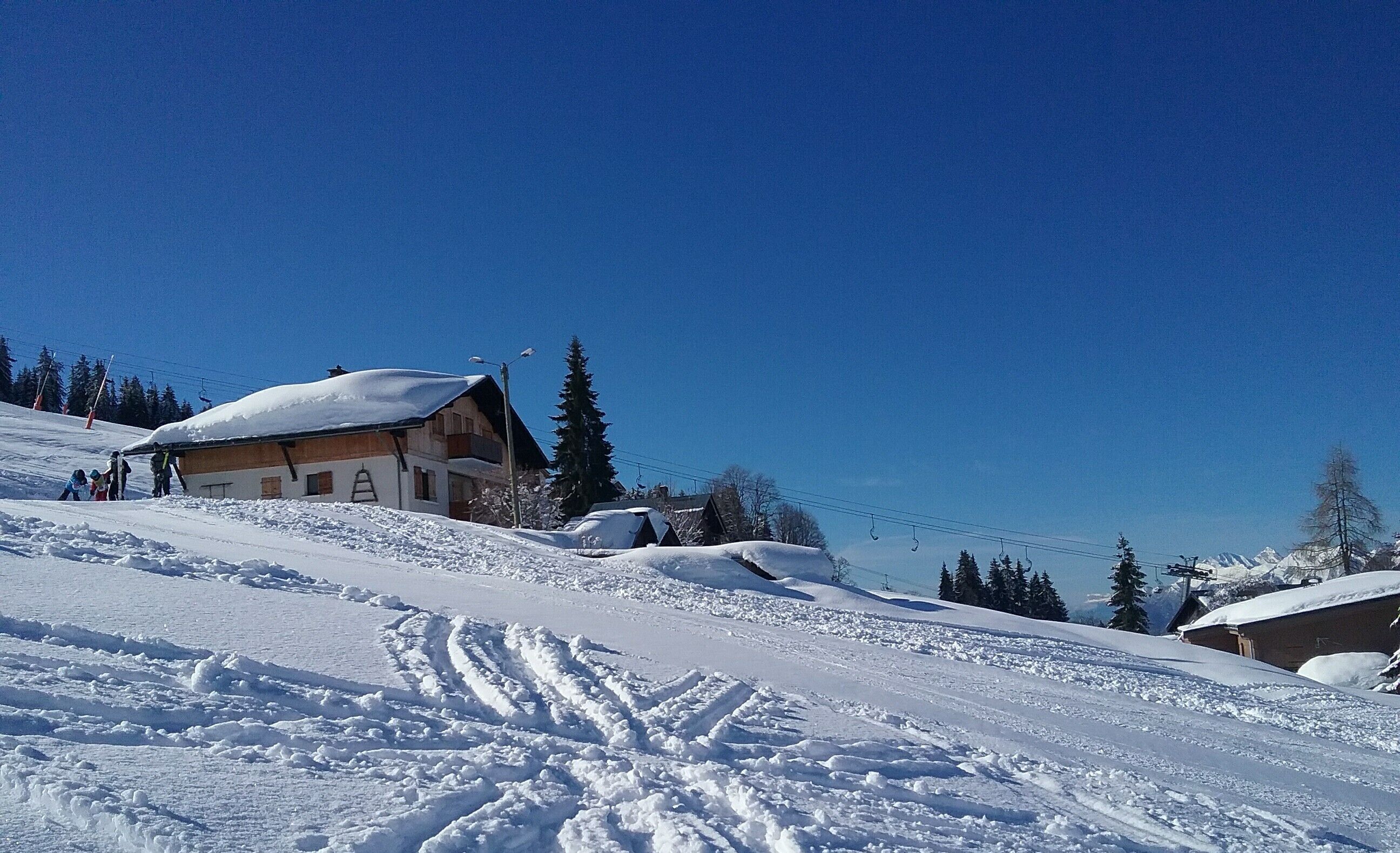 Ein mit Schnee bedeckter Ski-Hang mit einem Holzbau, einer Seilbahn und Bäumen.