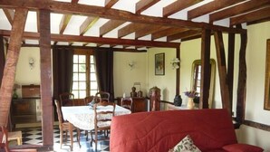 A room with a red sofa, a dining table with chairs, and a checkered floor. - TRADITIONAL GITE NORMAND (La Noë-Poulain)