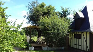 A garden with a wooden pergola, a small shed, and a variety of trees and shrubs. - TRADITIONAL GITE NORMAND (La Noë-Poulain)