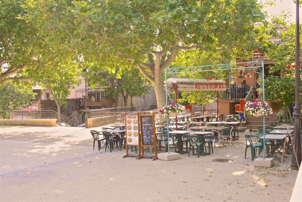 An outdoor cafe with tables and chairs under a tree, a signboard with menu items, and a staircase leading to a building with a sign that reads "RESTAURANT". - Le mas des oliviers de Rustrel with swimming pool (Rustrel)